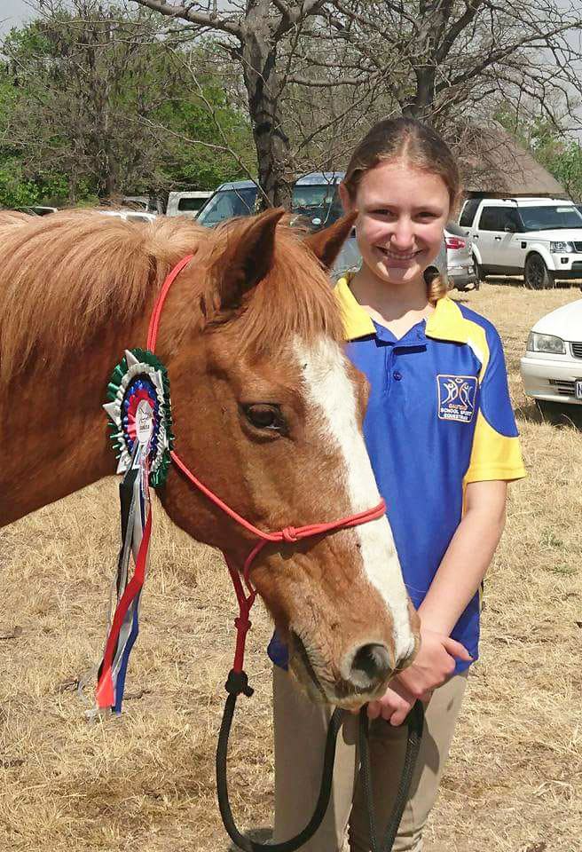 Young rider with her pony and a fistful of rosettes